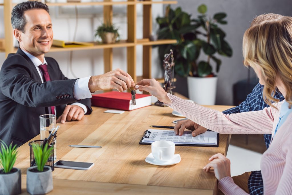 partial view of couple getting keys from new home from realtor in real estate agency office