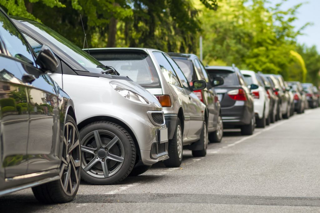 Rows of cars parked on the roadside in residential district. Small car parked between other cars