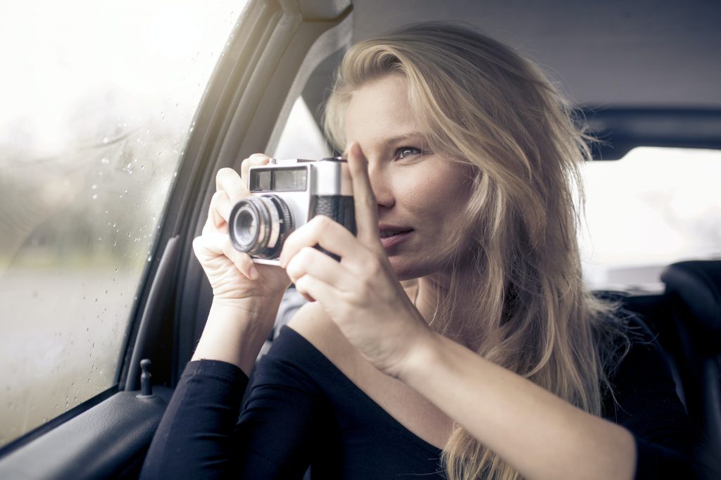 Woman sitting in car taking picture with camera